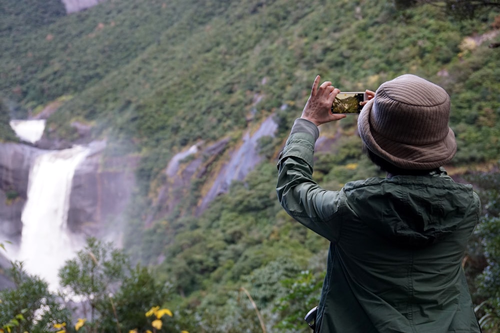 Hombre con chaqueta negra tomando fotos de cascadas durante el día