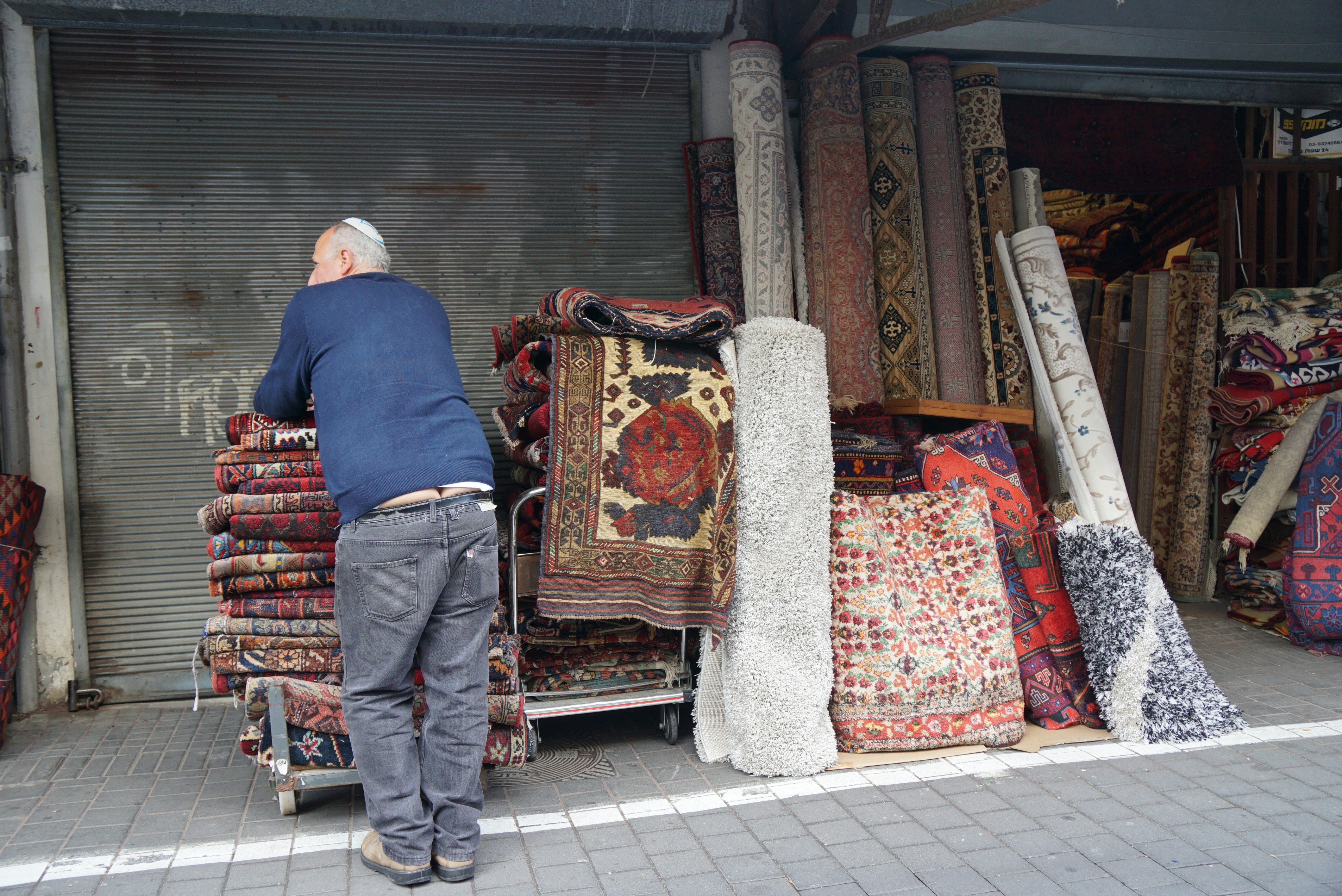 man in blue dress shirt and white pants standing on red and brown floral area rug