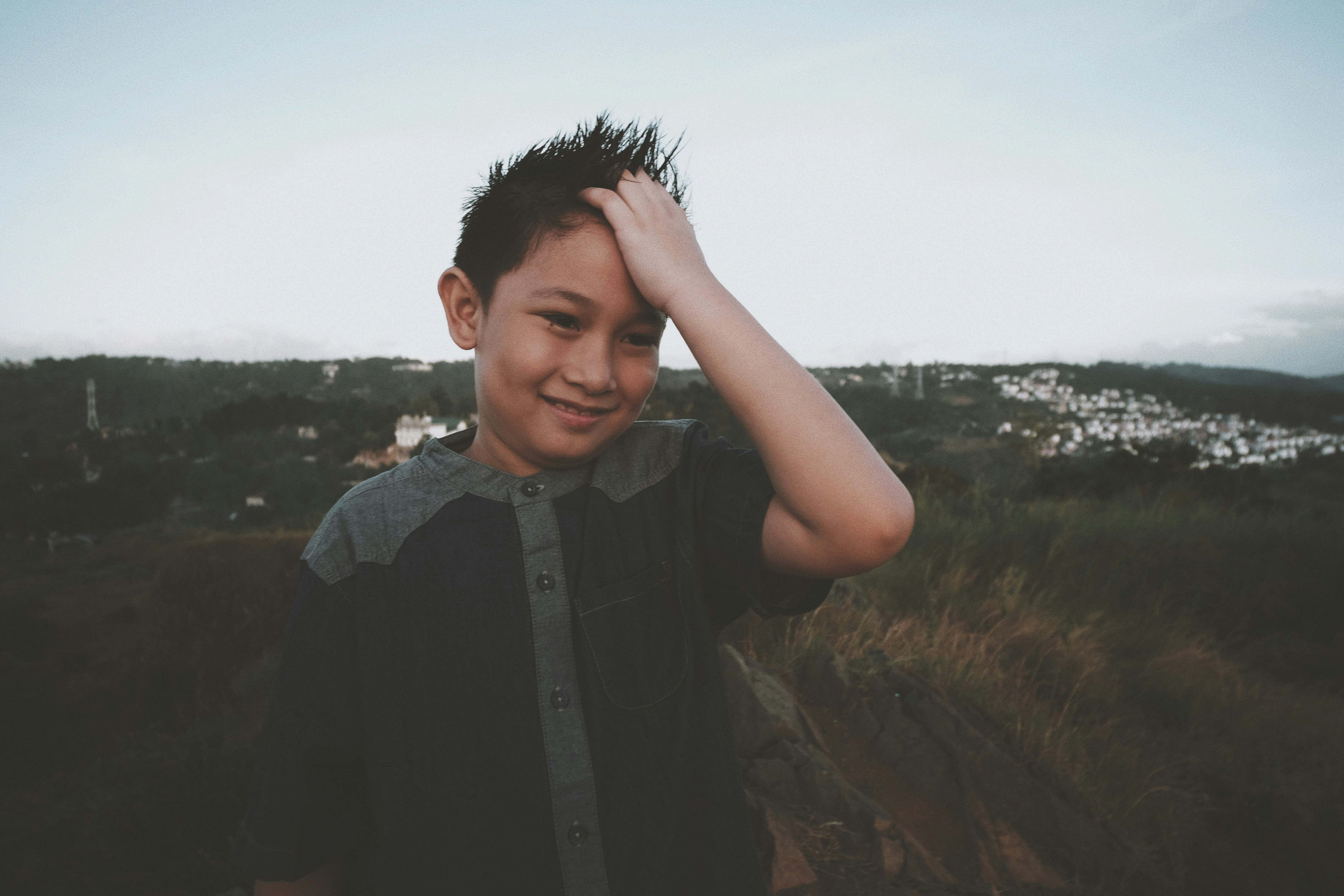 a young boy standing in a field with his hands on his head