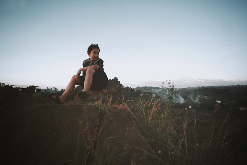 a boy sitting on a rock in a field