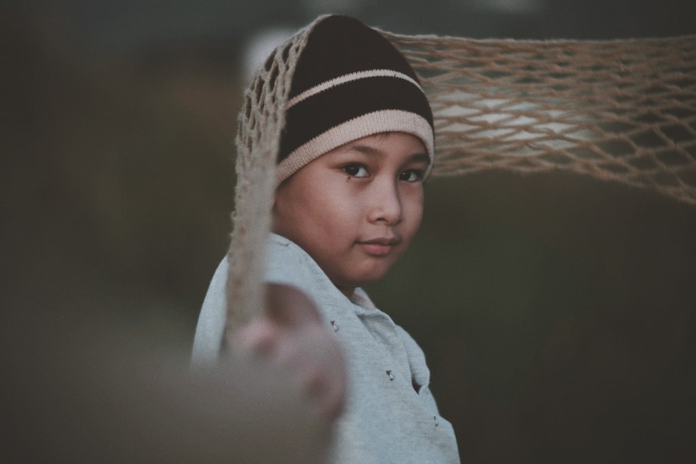 a young boy wearing a beanie and holding a hammock