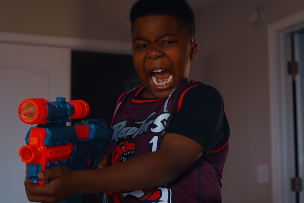 boy in black and red crew neck t-shirt holding red and black toy gun