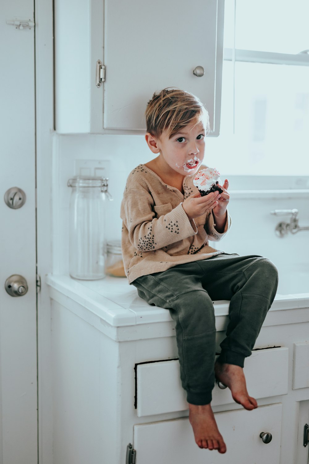 boy in brown sweater sitting on white ceramic sink