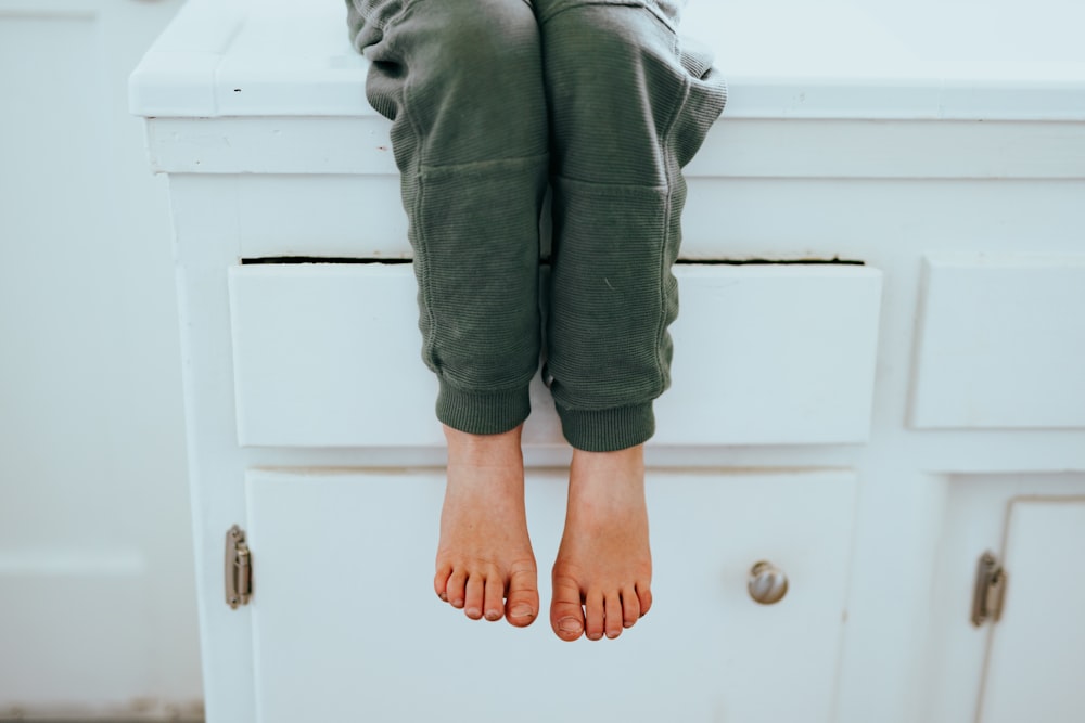 person in gray denim jeans standing on white wooden cabinet