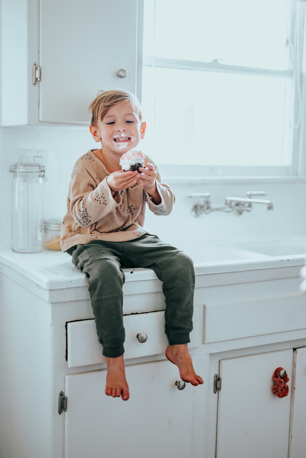 boy in brown sweater sitting on white ceramic sink