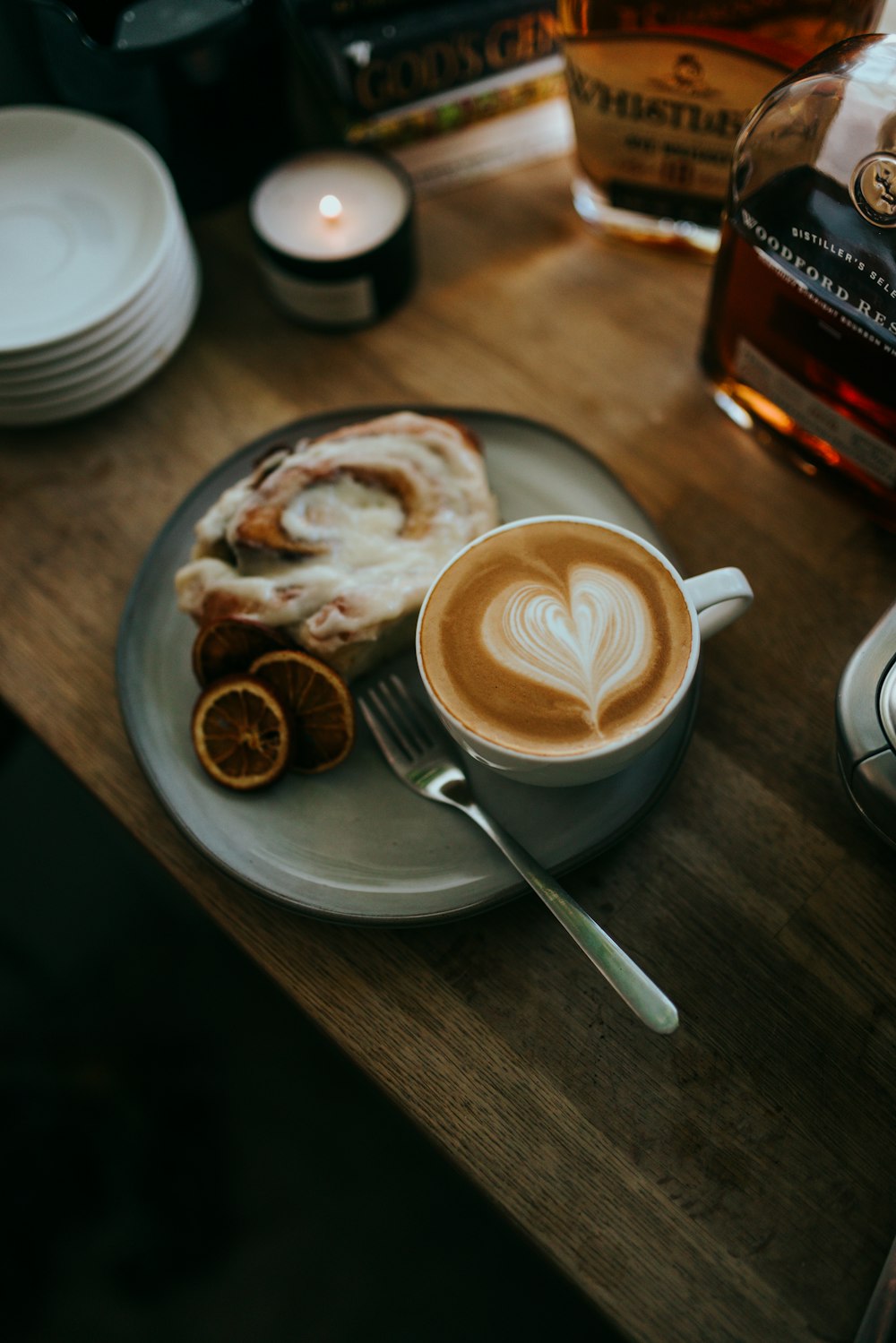 cappuccino in white ceramic cup on saucer beside stainless steel spoon