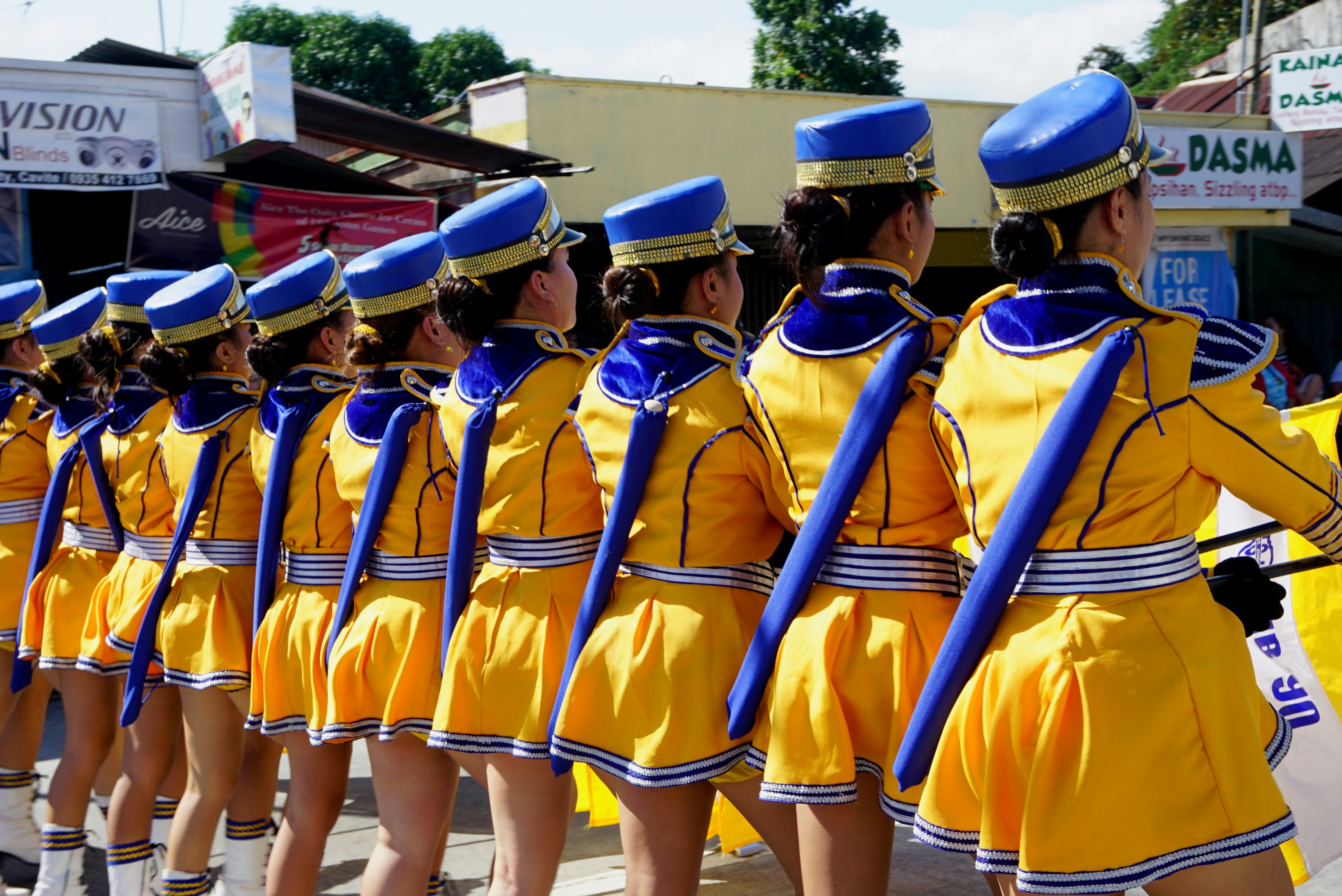 Marching band in short yellow skirts on the main street, taken from the back.