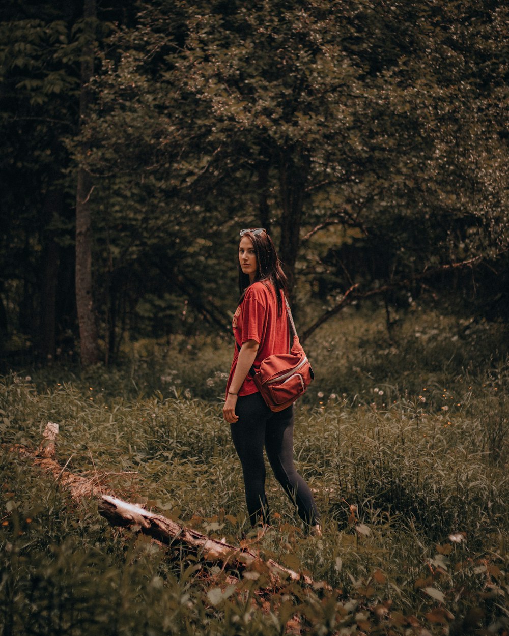 woman in red long sleeve shirt and black pants standing on brown log during daytime