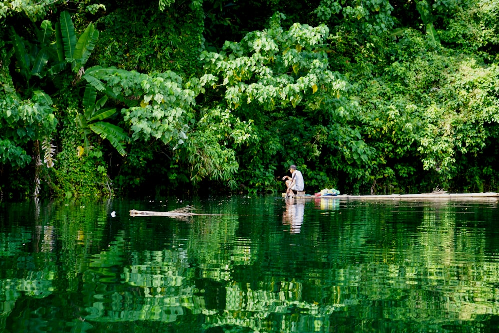 man in white shirt and black pants sitting on brown wooden dock during daytime