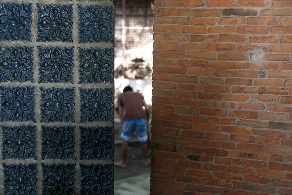 man in blue t-shirt standing beside brown brick wall