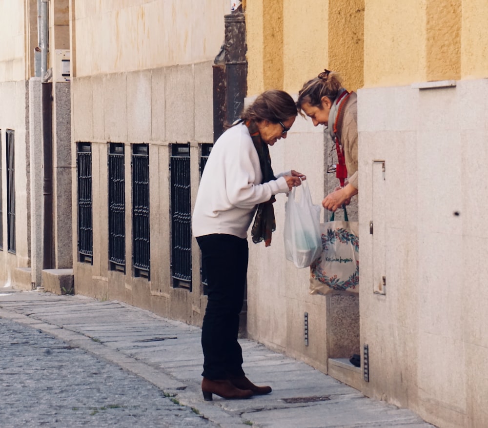 Donna in camicia bianca a maniche lunghe e pantaloni neri in piedi sul marciapiede durante il giorno