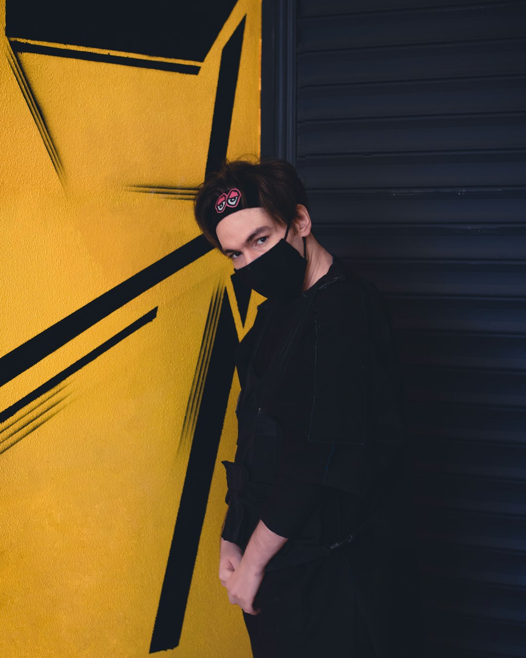 woman in black coat standing beside yellow wall