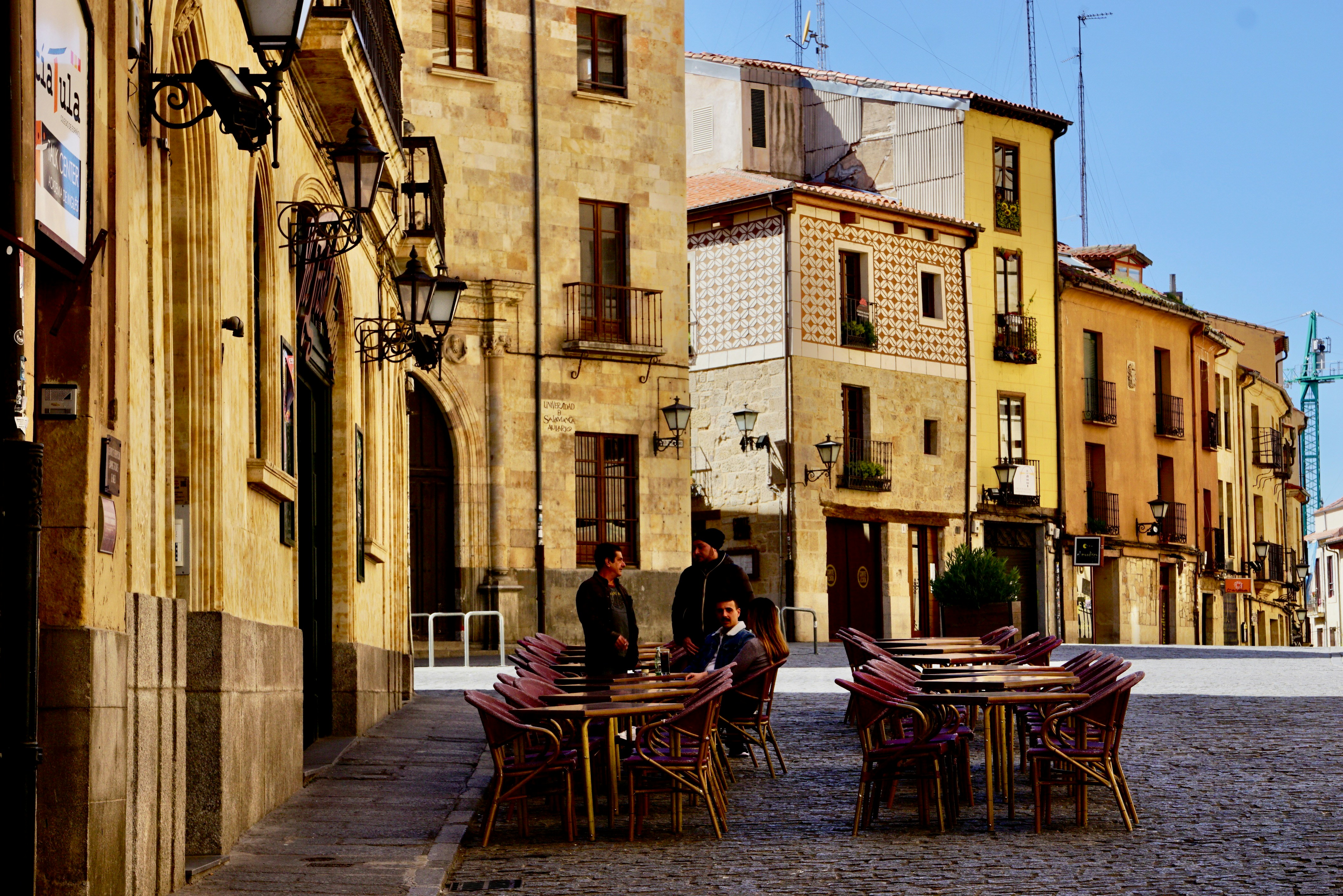 man and woman sitting on brown wooden chairs near brown concrete building during daytime