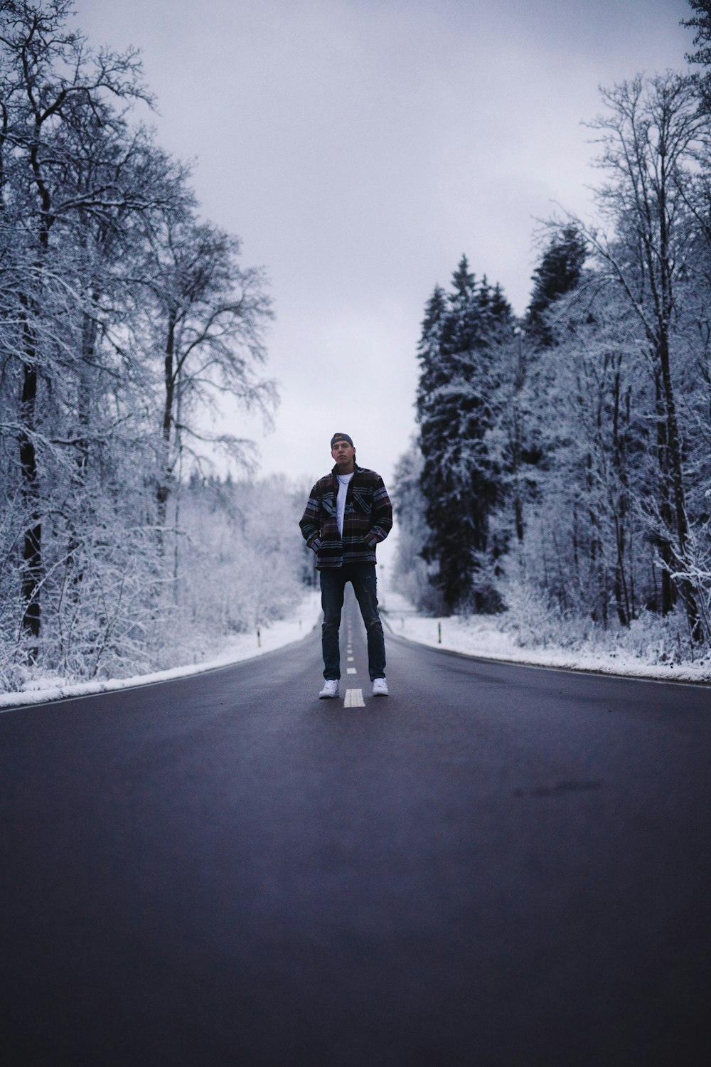 woman in black coat standing on road between trees covered with snow during daytime