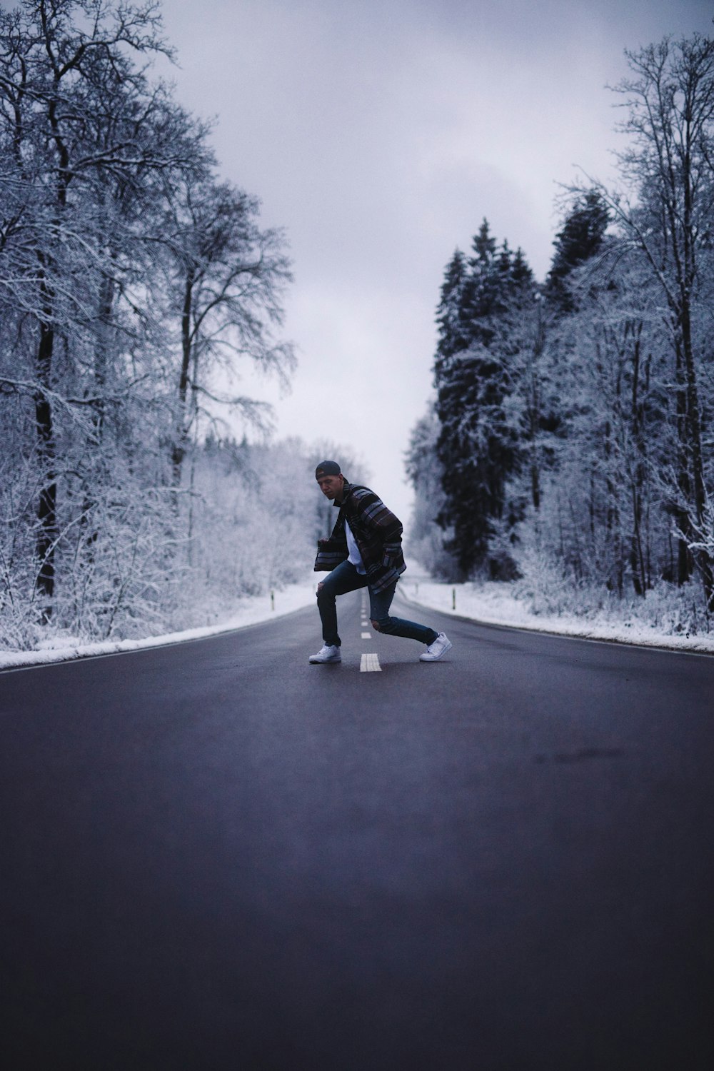 man in black jacket and blue denim jeans riding on black skateboard on snow covered road