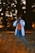 A person in casual attire is standing in a natural setting, holding a camera up to their eye, capturing a photograph. The background features blurred trees, creating a bokeh effect with warm-toned lighting.