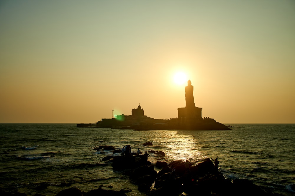 silhouette of lighthouse on rock formation near body of water during sunset