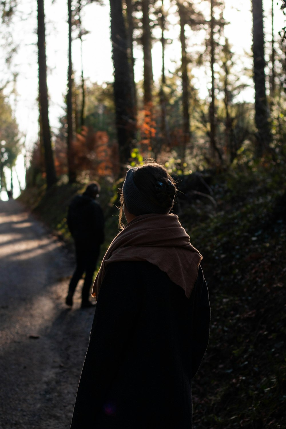 woman in brown hoodie walking on pathway in between trees during daytime