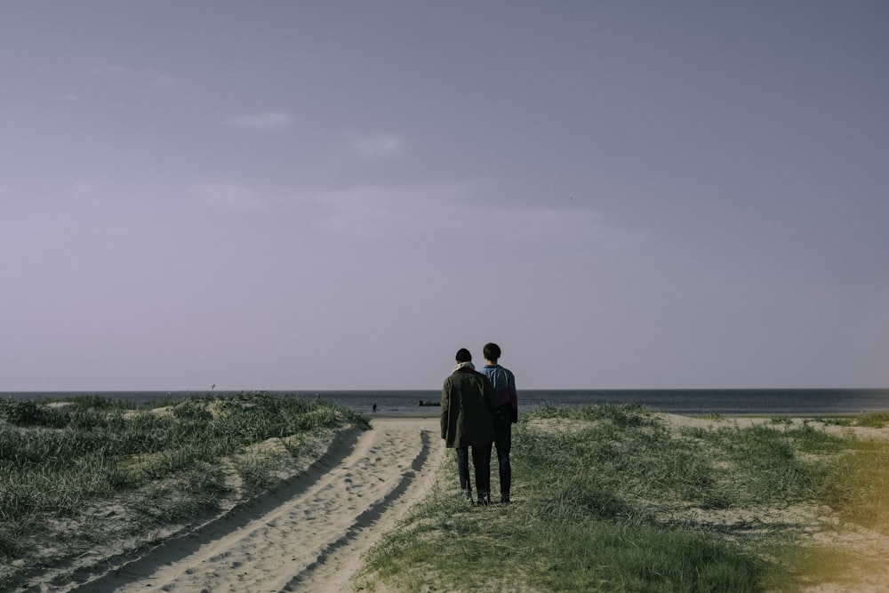 2 men walking on green grass field near sea during daytime