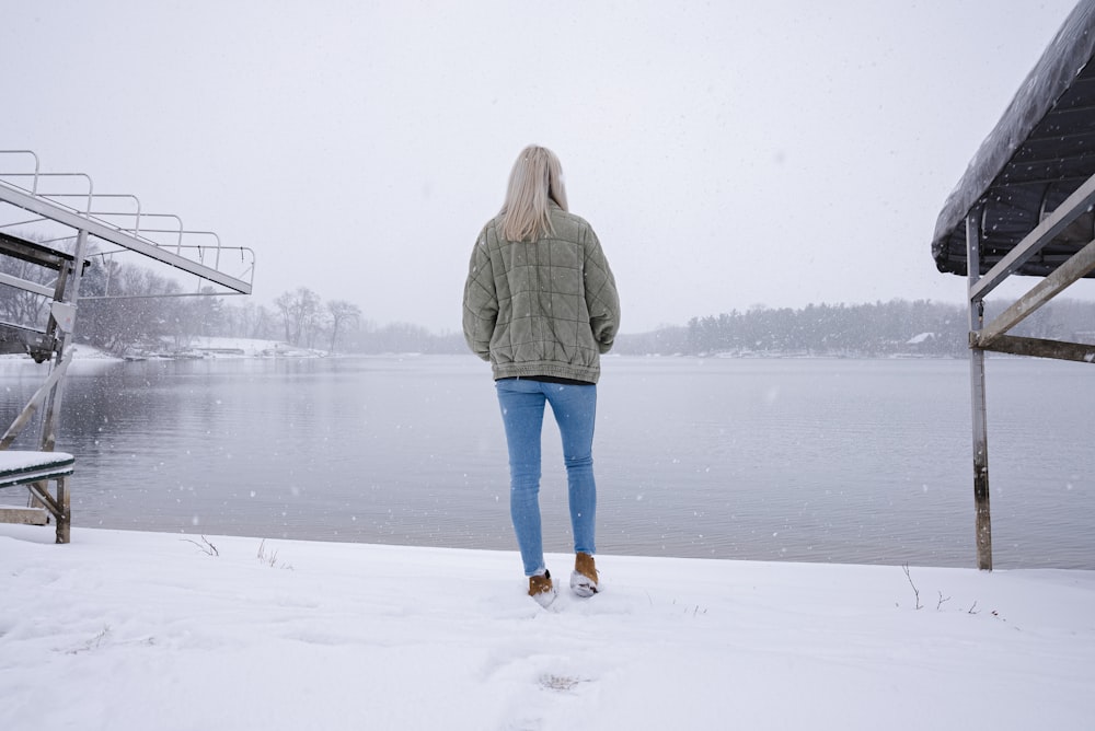 Donna in giacca grigia e jeans di jeans di jeans blu in piedi sul terreno coperto di neve durante il giorno