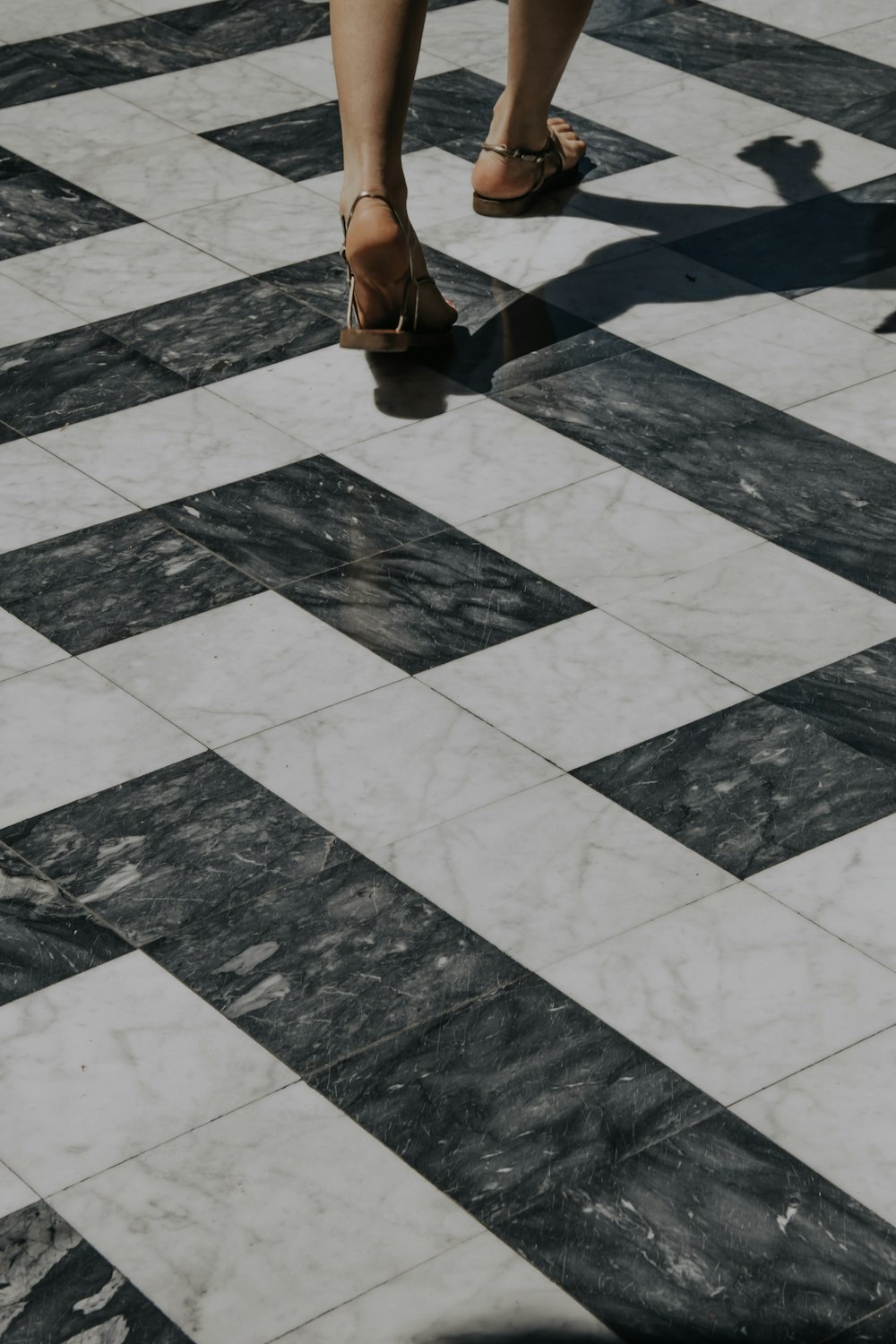 person in brown pants and brown shoes standing on gray and white floor tiles