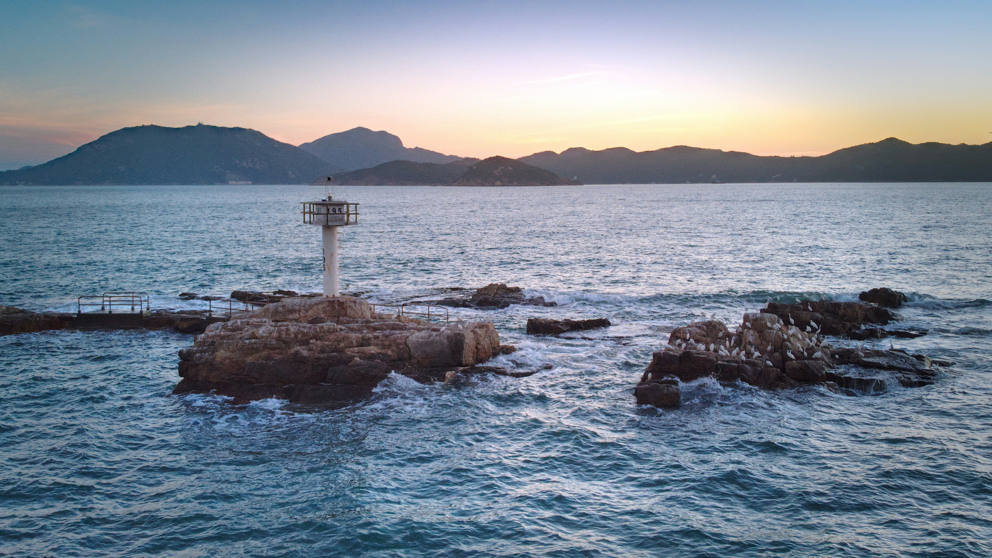 White and red lighthouse on brown rock formation near body of water ...