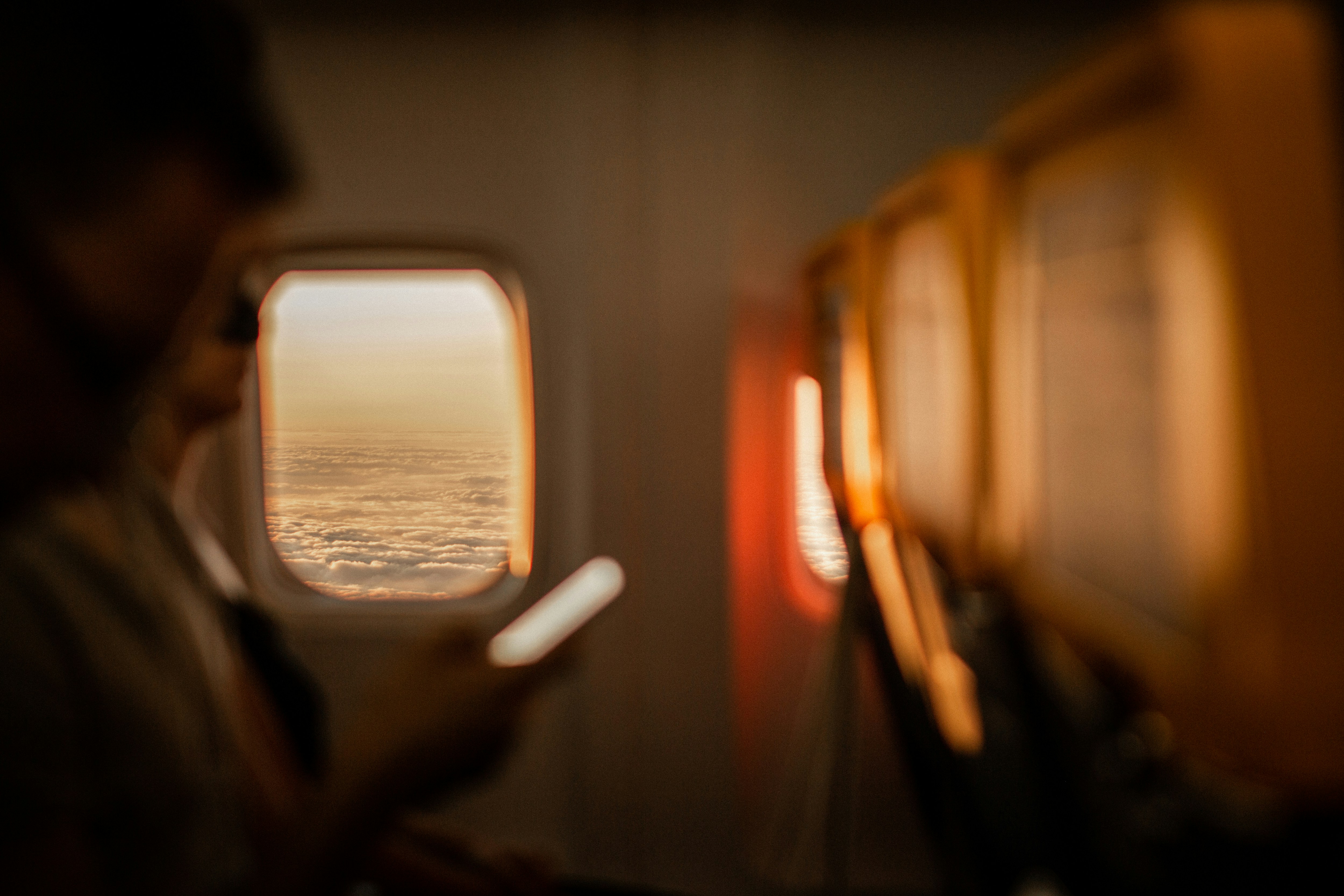airplane passenger looking out window holding smartphone