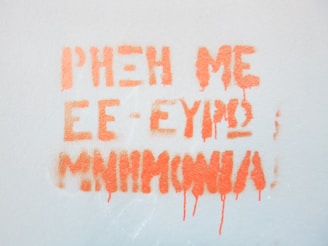 Orange graffiti text is sprayed on a light gray wall. The text appears smudged with some paint drips.