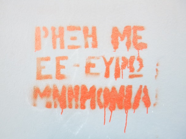 Orange graffiti text is sprayed on a light gray wall. The text appears smudged with some paint drips.