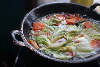 A close-up of a well-seasoned cast iron pan sizzling with vegetables on a stovetop.