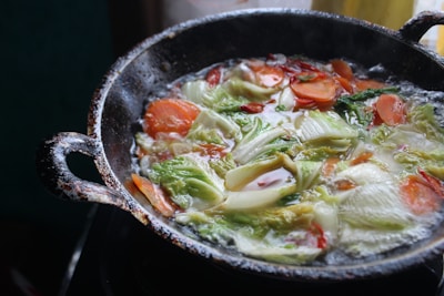 A cast iron skillet sizzling with fresh vegetables on a stove surrounded by potted plants.