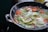A close-up of a cast iron skillet with fresh vegetables sizzling inside.