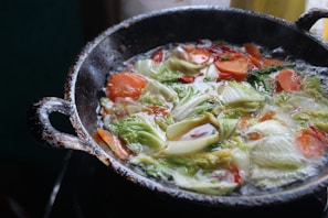 A close-up of a sturdy cast iron skillet heating on a stove with fresh vegetables nearby.