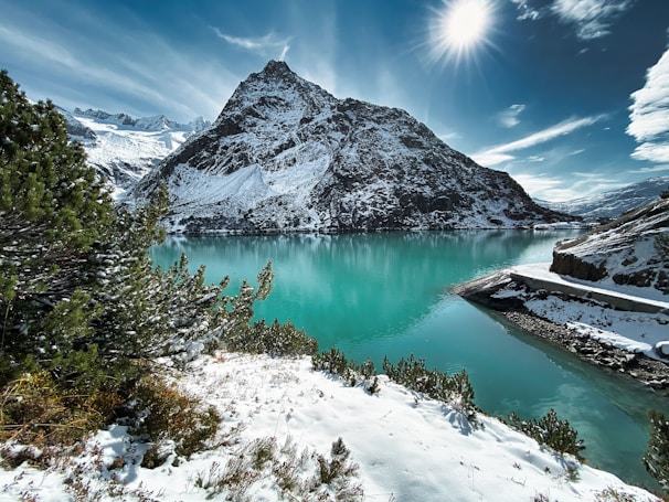 A serene view of the turquoise waters of Lake Nahuel Huapi surrounded by snow-capped mountains at sunrise.