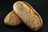 Two loaves of bread encrusted with sesame seeds and other seeds are placed together on a dark surface. The bread has a golden-brown crust and appears freshly baked.