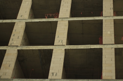 A partially constructed building frame with exposed concrete and brickwork, featuring rectangular openings for windows or rooms. The structure is in an early stage of development, with visible building materials and construction markings.