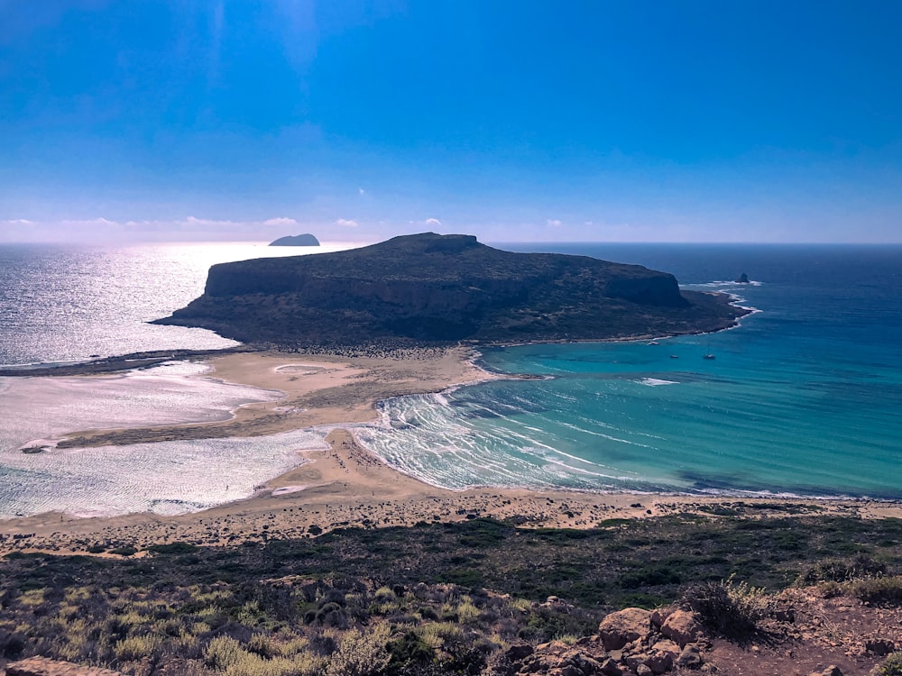 Montaña verde y marrón al lado del cuerpo de agua durante el día