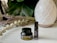 A small black container labeled CBD Muscle Rub and a black roller bottle labeled Calm are placed on a white surface. Behind them, there is a white, patterned diffuser. There are also dried lavender and eucalyptus stems arranged on the left side. In the background, large green leaves provide a soothing backdrop.