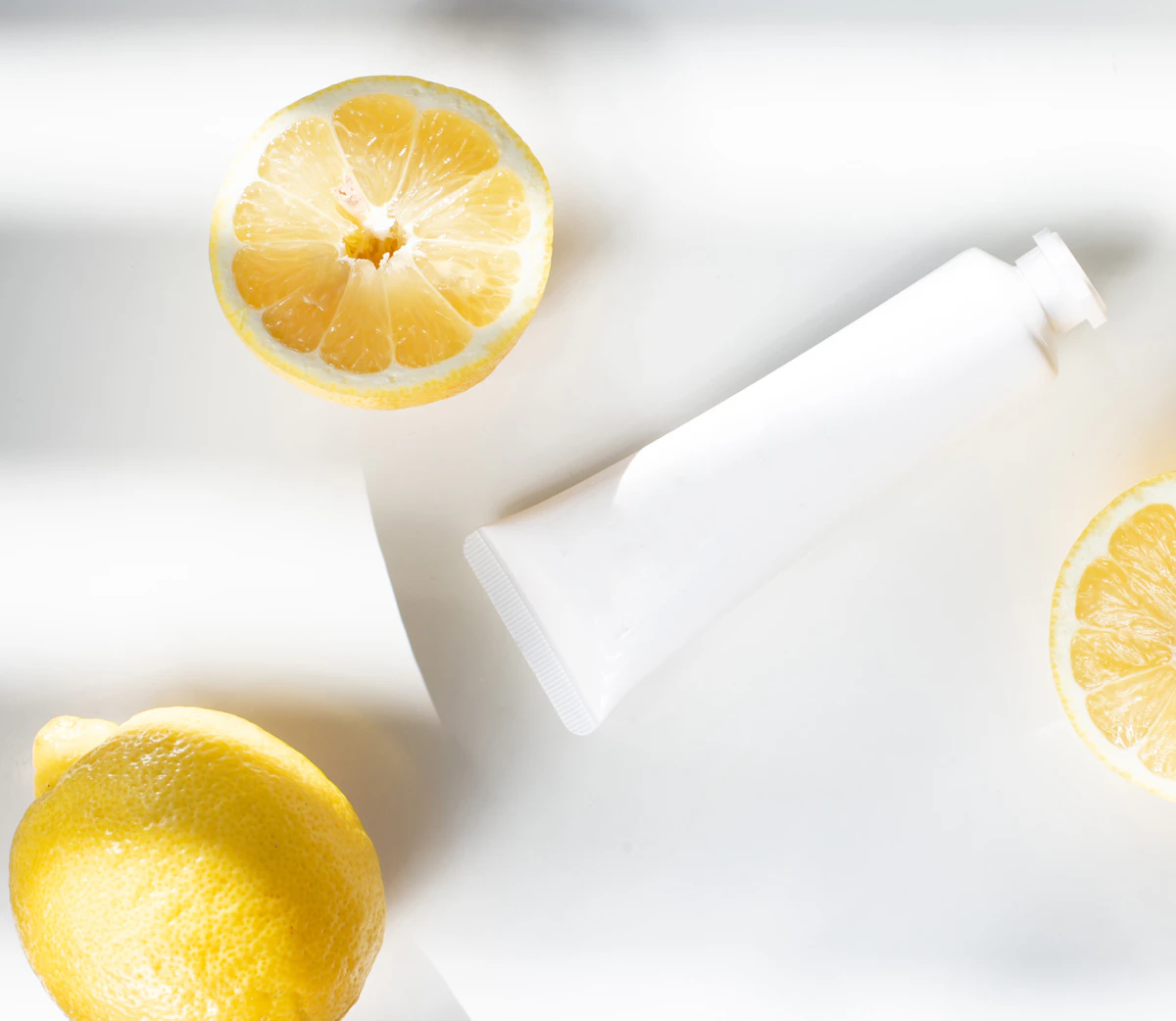 Sliced lemon beside a white ceramic container of facial oil styled on a light textured surface