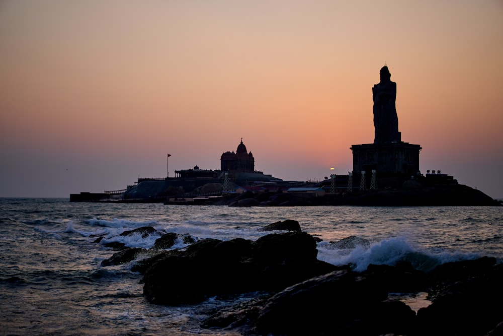 silhouette of lighthouse near body of water during sunset