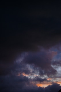 Dark, ominous clouds dominate the sky, with subtle hints of blue, orange, and pink peeking through, suggesting a turbulent weather condition or approaching storm.