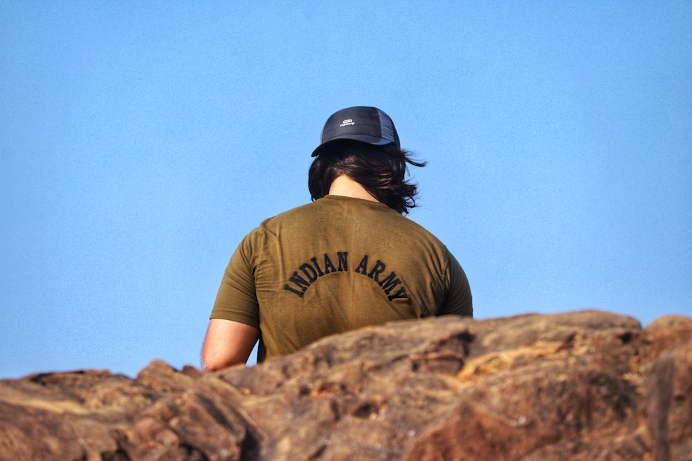 man in brown crew neck t-shirt and black cap sitting on brown rock during daytime