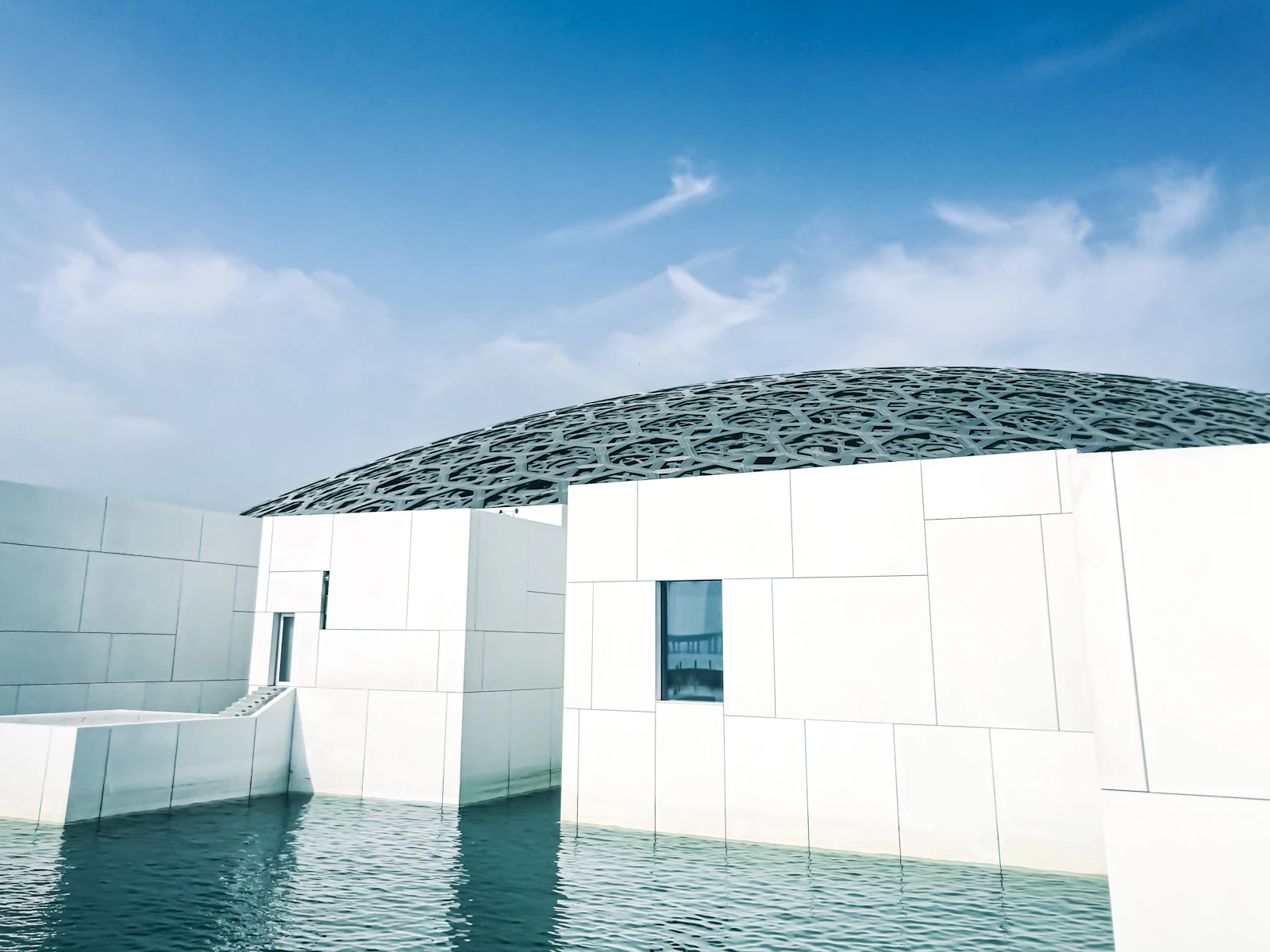 Louvre Abu Dhabi dome and white galleries beside the water