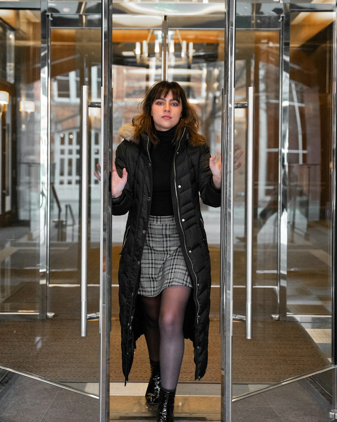 woman in black leather jacket and black mini skirt standing beside glass wall
