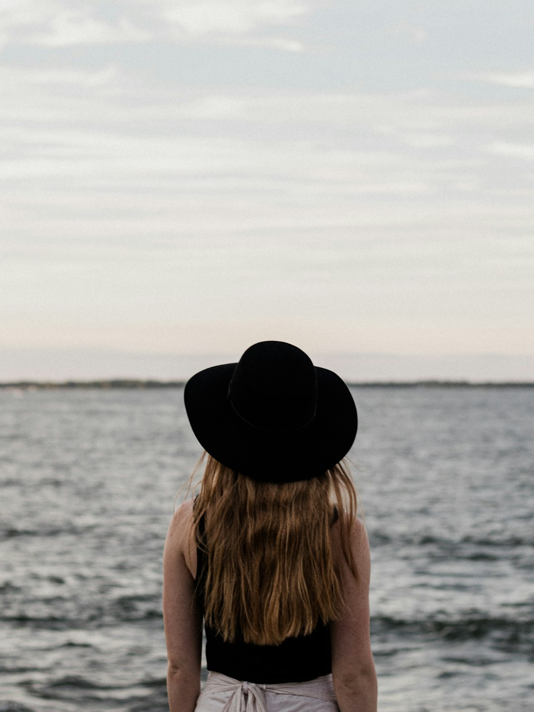 woman in black fedora hat near body of water during daytime