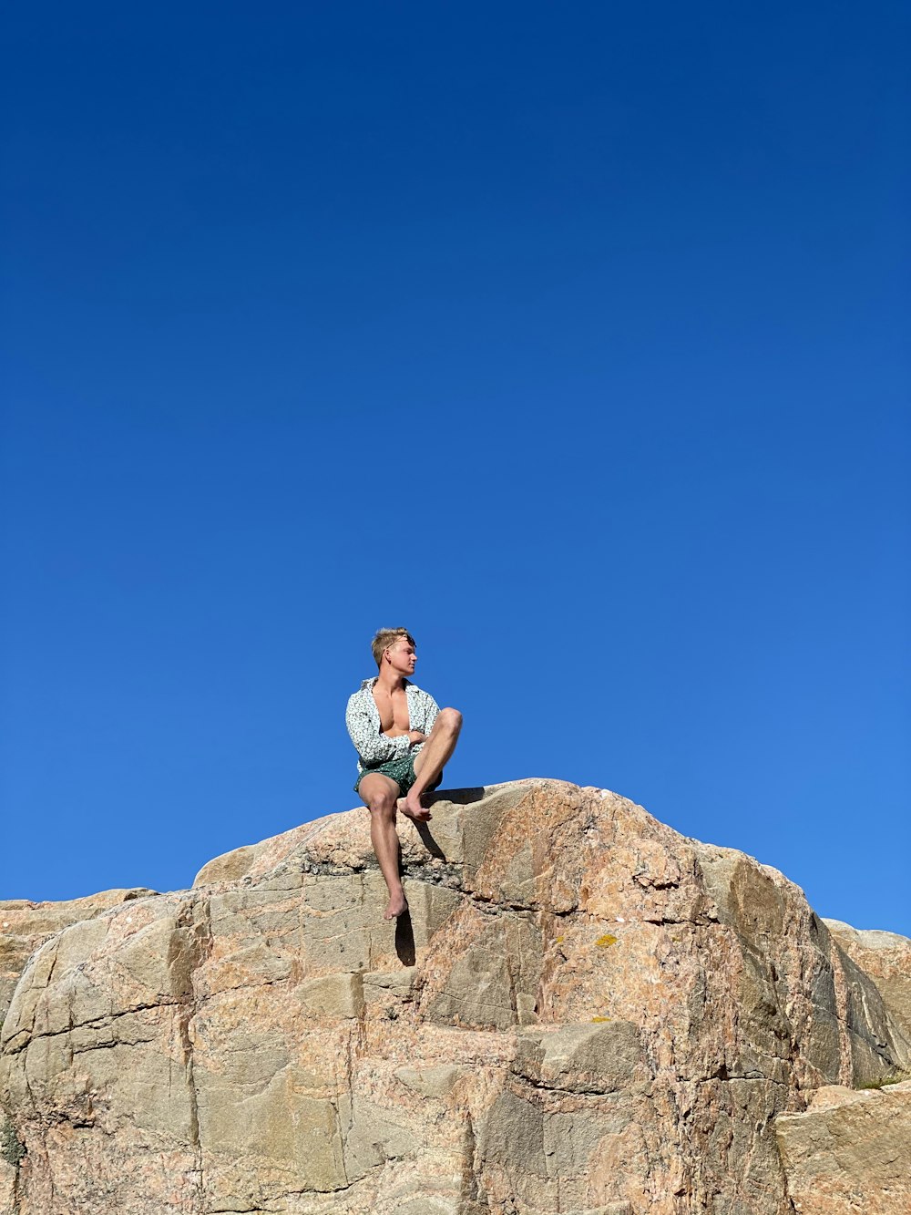 woman in pink tank top and black shorts sitting on brown rock during daytime