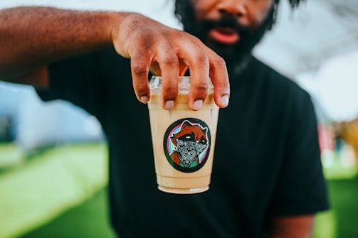 Hands holding a Dulaplast cup filled with a refreshing beverage outdoors.