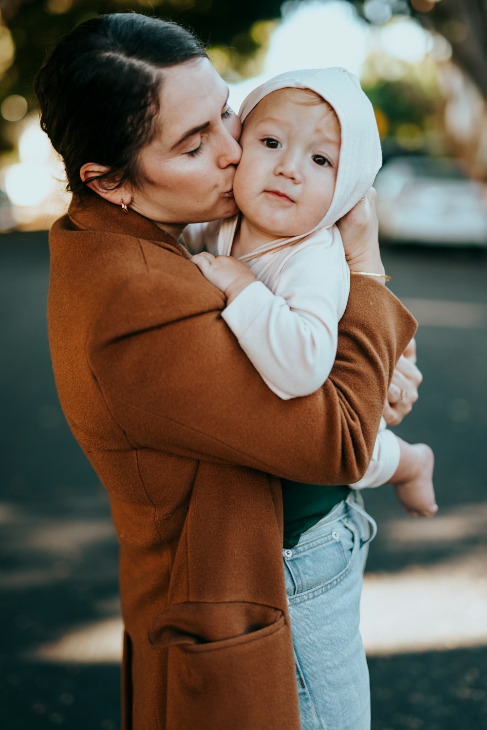 woman in brown coat carrying baby in white knit cap