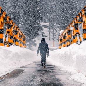 man in black jacket walking on snow covered road during daytime