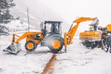 Heavy machinery shaping terrain at a ski resort construction site surrounded by pine trees.